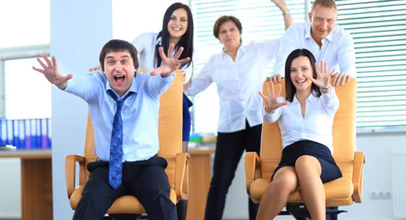 Happy office employees having fun at work in an office chair race Happy employees showing enthusiasm