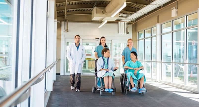 Medical Team With Patients On Wheelchairs At Hospital Corridor Team of doctors and nurses wheeling patients down a hallway